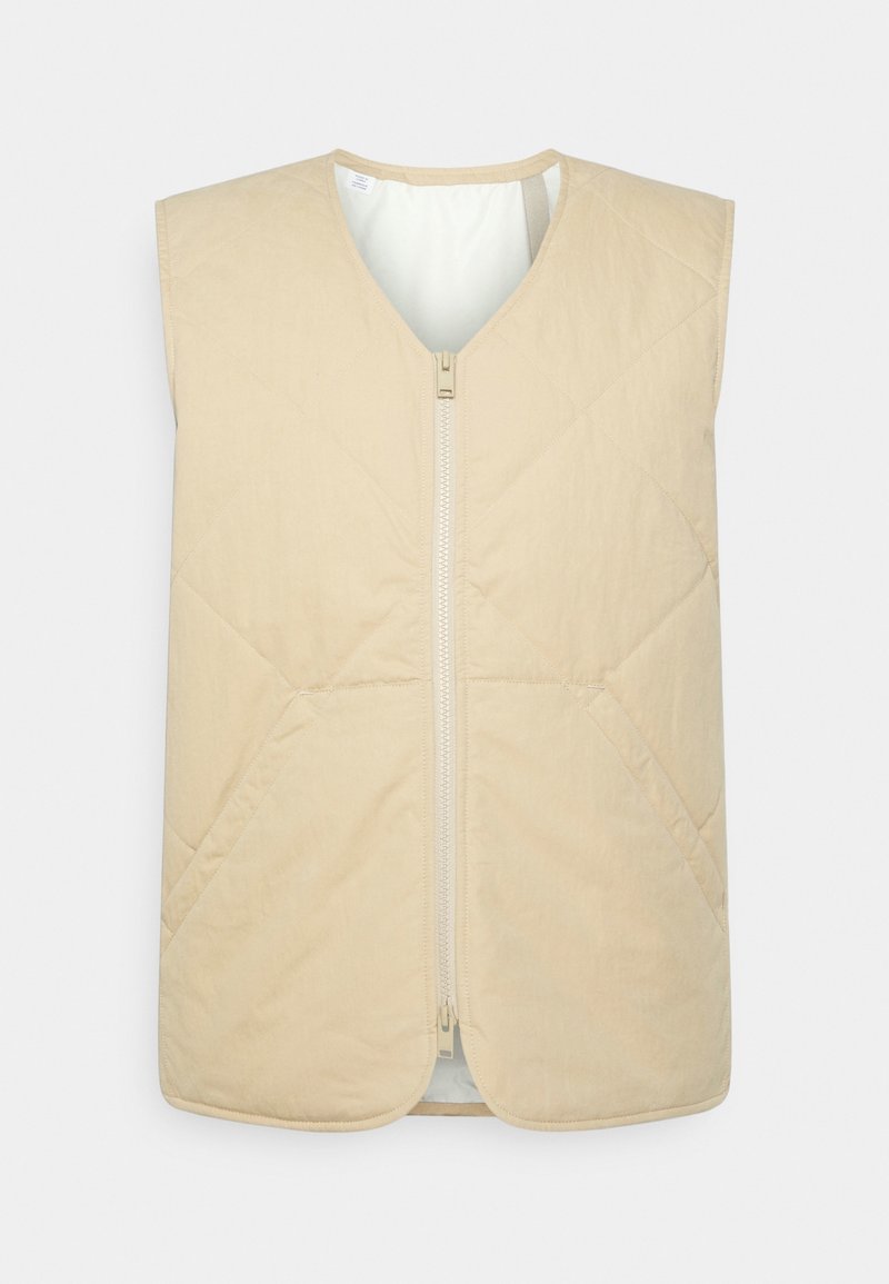 Beige vadderad väst med V-hals, ärmlös design, framzippering och mjuk textur, med diagonala sömmar.