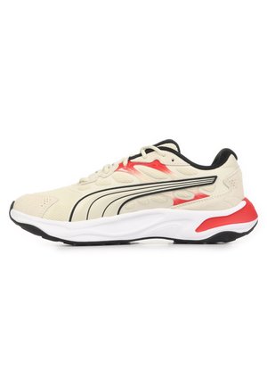 Chaussure de sport beige clair avec accents noirs et rouges, semelle blanche, et logo Puma noir sur le côté, présentée sur un fond blanc.