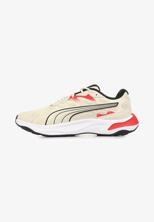 Chaussure de sport beige clair avec accents noirs et rouges, semelle blanche, et logo Puma noir sur le côté, présentée sur un fond blanc.