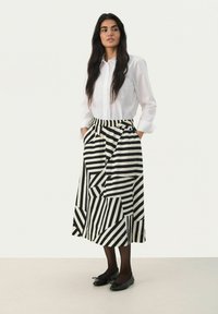 Jupe rayée noire et blanche avec des motifs géométriques, associée à une chemise blanche à boutons. La jupe comprend des poches et a une coupe décontractée.