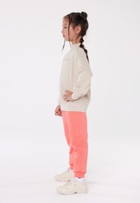 Beige sweatshirt with ribbed cuffs, paired with bright pink sweatpants and beige sneakers. Simple design, relaxed fit, smooth texture.