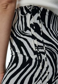 Zwart-witte zebra-print stof met een aansluitend ontwerp en een gestrikte taille. Close-up toont een gladde textuur en een gedetailleerd patroon.
