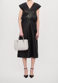 Czarna skórzana sukienka z krótkimi rękawami typu cap, dekoltem w kształcie litery V oraz rozkloszowanym krojem. Szara torebka z zaokrąglonymi uchwytami i metką, zestawiona z czarnymi spiczastymi szpilkami.