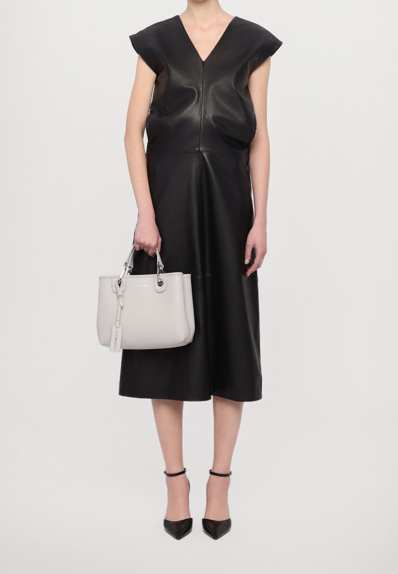 Czarna skórzana sukienka z krótkimi rękawami typu cap, dekoltem w kształcie litery V oraz rozkloszowanym krojem. Szara torebka z zaokrąglonymi uchwytami i metką, zestawiona z czarnymi spiczastymi szpilkami.