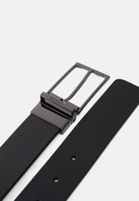 Ceinture en cuir noir dotée d'une boucle en métal rectangulaire avec une finition mate. Le design comprend des trous pour des ajustements, mettant en valeur une texture lisse.