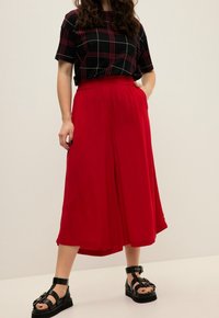 Rode wijde culottes met een gladde textuur, een aansluitende tailleband, gecombineerd met een zwart geruit top. Zwarte sandalen met bandjes maken de outfit compleet.