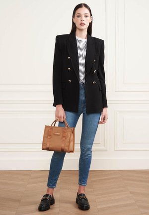 Blazer noir à double boutonnage, t-shirt rayé, jeans skinny bleus, sac fourre-tout marron avec poignées, et mocassins noirs. Fond de sol en bois plat.