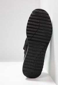 Svart skosula med texturerade greppmönster; har en gummi sula och mjukt övermaterial, designad för komfort och hållbarhet.