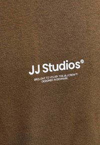 Tissu marron avec texte blanc disant "JJ Studios. Présenté par l'équipe J&J. Conçu au Danemark."