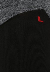 Calze a coste nere e grigie con una parte superiore grigia e una "L" rossa sul lato, che indica l'orientamento per il piede sinistro. Morbido tessuto a maglia.
