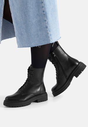 Czarne skórzane botki z sznurowadłami i bocznymi zamkami. Gruba gumowa podeszwa z teksturowanym bieżnikiem. Gładkie wykończenie i zaokrąglony kształt czubka.