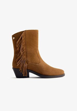 Botín de ante marrón con detalle de flecos en los laterales, puntera redondeada y tacón bajo tipo bloque. Presenta una textura suave y un diseño limpio y sencillo.