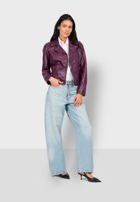 Fialová kožená motorkářská bunda se zipy, pod ní bílá košile, doplněná světle modrými širokými džínami a černými botami s špičatou špičkou.