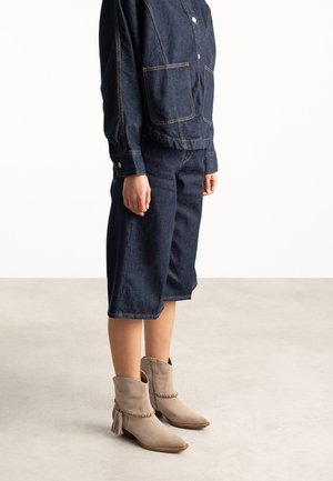 Person wearing dark blue denim jacket and matching wide-leg cropped pants with light beige suede ankle boots.