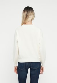 Biała bluza z długim rękawem, okrągłym dekoltem i ściągaczem w pasie. Połączona z ciemnoniebieskimi dopasowanymi dżinsami. Minimalistyczny design bez wzorów.