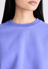 Sudadera de algodón morado con cuello redondo acanalado, textura suave y diseño minimalista. Sin patrones ni gráficos visibles.