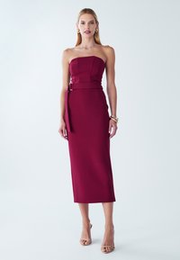 Bordo brez naramnic obleka z oblikovanim korzetom in pasnim detajlom v pasu. Gladek, oprijet material segaja do sredine meč.