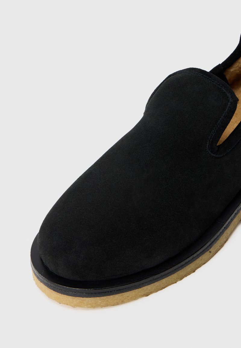 Scarpa slip-on in suede nero con punta arrotondata, dotata di una morbida fodera interna e di una soletta beige a contrasto per texture e durata.