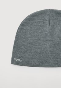 Szary, dzianinowy beanie z delikatnym prążkowaniem i małym haftowanym logo "HUGO" blisko krawędzi na białym tle.