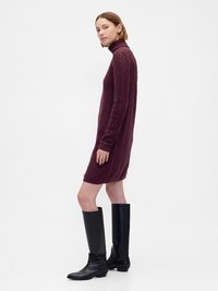 Rochie tricotată de culoare burgund cu guler înalt, având un model de tricotaj cu cablu. Modelul poartă cizme negre din piele până la genunchi pentru contrast.