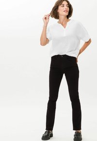 Jeans de mezclilla negra con un ajuste slim, que cuentan con una cintura de altura media y un cierre de botón clásico. Combinados con una blusa blanca de mangas cortas.