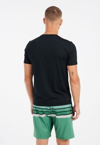 Zwarte T-shirt met korte mouwen en een ronde hals, gecombineerd met groene shorts met horizontale strepen in zwart, wit en lichtgroen.
