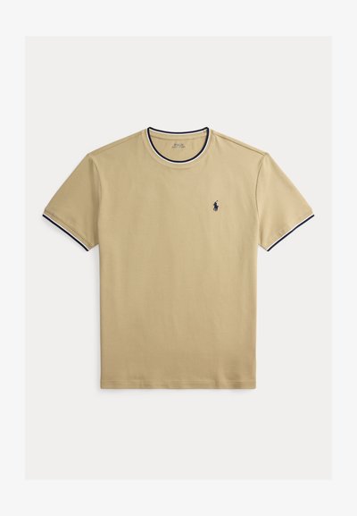 T-shirt en coton beige avec un col rond, bordure bleu marine au col et aux manches, et un petit logo bleu marine sur le côté gauche de la poitrine. Texture lisse.