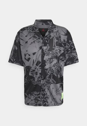 Chemise en maille à manches courtes noire et grise avec un motif abstrait, devant boutonné, col en pointe et petite étiquette vert néon près de l'ourlet.