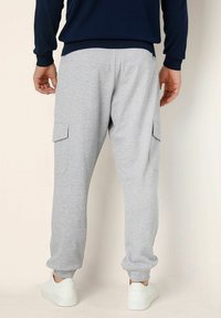 Grå cargobyxor i sweatmaterial med elastiska benslut, sidofickor och en avslappnad passform, i kombination med vita sneakers. Materialet ser mjukt och avslappnat ut.