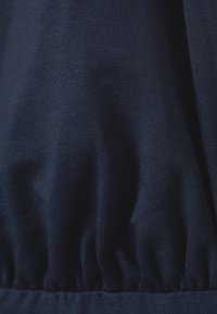 Tessuto blu navy con una superficie morbida e testurizzata. Presenta un dettaglio arricciato nella parte inferiore, che mette in evidenza una finitura liscia ed elastica.
