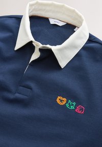 Maglietta da rugby blu navy con colletto bianco e volti ricamati di leone arancione, gatto verde e elefante rosa sul petto.