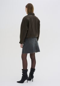 Brun kort jacka, svart mini denimkjol med franskant, svarta slouchy ankelstövlar, genomskinliga svarta strumpbyxor. Bakifrån.