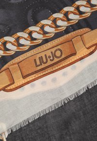 Sciarpa con sfondo nero e motivo a catena in oro e crema, rifinita con un'etichetta color sabbia con la scritta "LIU·JO". Tessuto leggero con bordi frangiati.