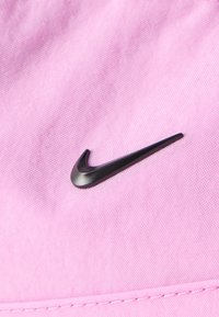 Fekete Nike pipa logó texturált világos rózsaszín anyagon, alul látható varrásokkal.