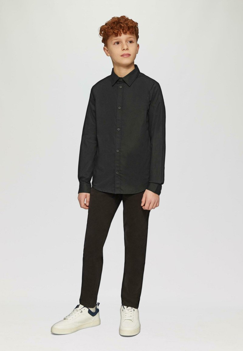 Zwart overhemden met kraag, gedragen met donkere broek en witte sneakers. Het overhemd heeft een gladde textuur en een slim-fit ontwerp.