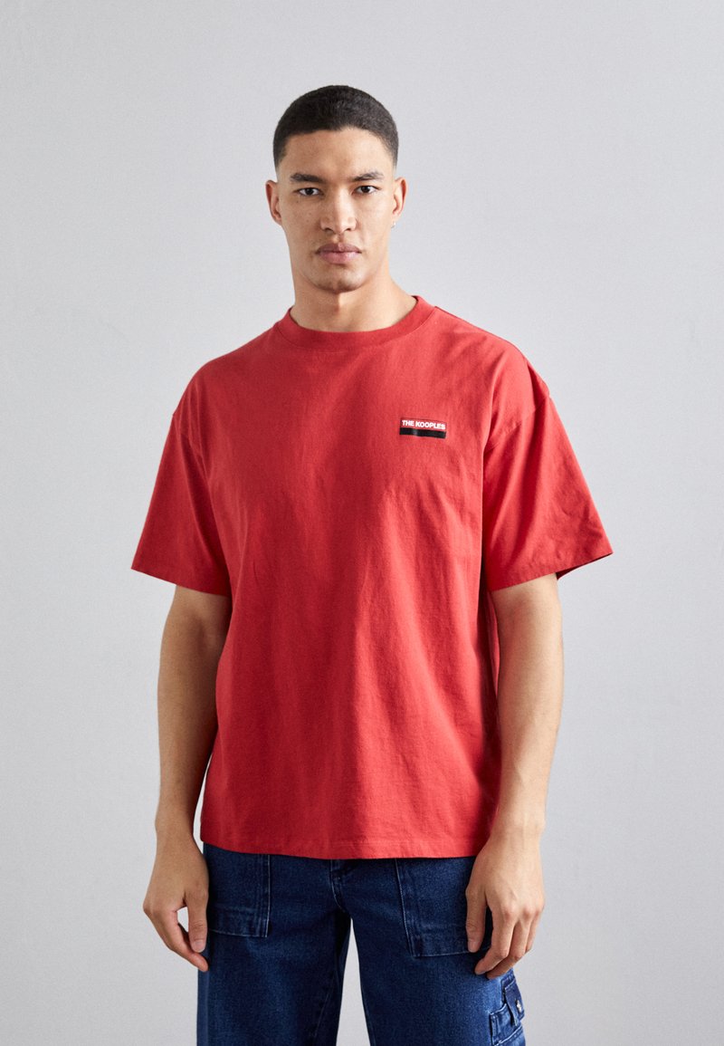 Rød bomuld t-shirt med korte ærmer og rund hals. Har et lille sort mærke på venstre brystområde. Enkel, afslappet pasform.