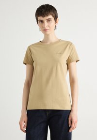 Khaki T-shirt met korte mouwen, gemaakt van katoen, met een ronde halslijn en geborduurd logo op de linker borst. Gepaarde met donkerblauwe jeans.