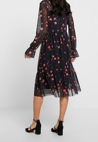 Abito nero a fiori con orlo a balze, maniche lunghe trasparenti e polsini arricciati. Presenta motivi floreali rossi e rosa su tessuto leggero.