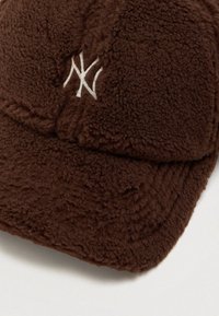Gorra de béisbol de forro marrón con el logo NY entrelazado en blanco bordado en el panel frontal, exhibida sobre una superficie blanca.