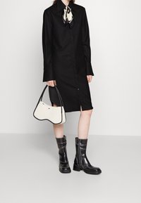 Svart skjortklänning med ränder och knäppning, kombinerad med svarta läderankelboots med vit sömnad och en vit handväska med en rundad design.