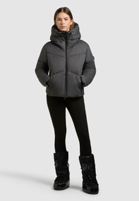 Giacca a vento grigia scura, con colletto alto, chiusura con zip e tasche laterali. Abbinata a leggings neri e stivali neri al ginocchio.