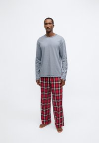 Grå tröja med lång ärm kombinerad med röda pyjamasbyxor i rutig design. Tyget verkar mjukt, med en ledig passform och subtil textur.