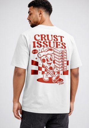 Mann trägt weißes T-Shirt mit rotem Cartoon-Pizzastück und hält gestapelte Pizzakartons, die mit Wochentagen und Text "Crust Issues." beschriftet sind