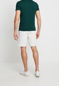 Camiseta de manga corta de color verde oscuro combinada con pantalones cortos blancos, hecha de algodón. Zapatillas blancas completan el conjunto, con un diseño simple y logotipos.