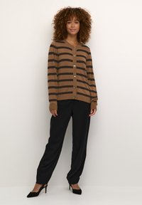 Bruine en zwarte gestreepte cardigan, met knoopsluiting en ribgebreide manchetten. Gepaard met zwarte broeken en zwarte hakken. Gestructureerde stof.