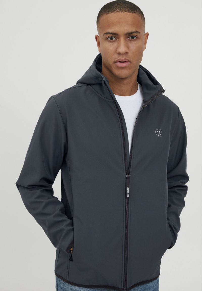 Veste zippée grise avec capuche, présentant une texture lisse, des poches avant et un petit logo sur la poitrine. Détail sur la fermeture éclair visible.