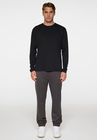 Musta pitkähihainen paita, jossa on pyöreä kaula-aukko, yhdistettynä harmaisiin collegehousuihin, joissa on joustavat mansetit, ja valkoisiin lenkkareihin. Sujuva pinta.