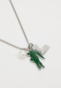 Collar de cadena de plata con un charm de cocodrilo verde, un acento de perla y un charm en forma de letra "L" en plata. Diseño texturizado y juguetón.