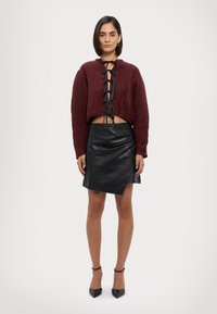 Burgundijas krāsas īss korduroja džemperis ar melniem mežģīņu detaļām, apvienots ar melnu mākslīgās ādas apjozošu svārku. Melni potītes siksniņš zābaki pabeidz izskatu.