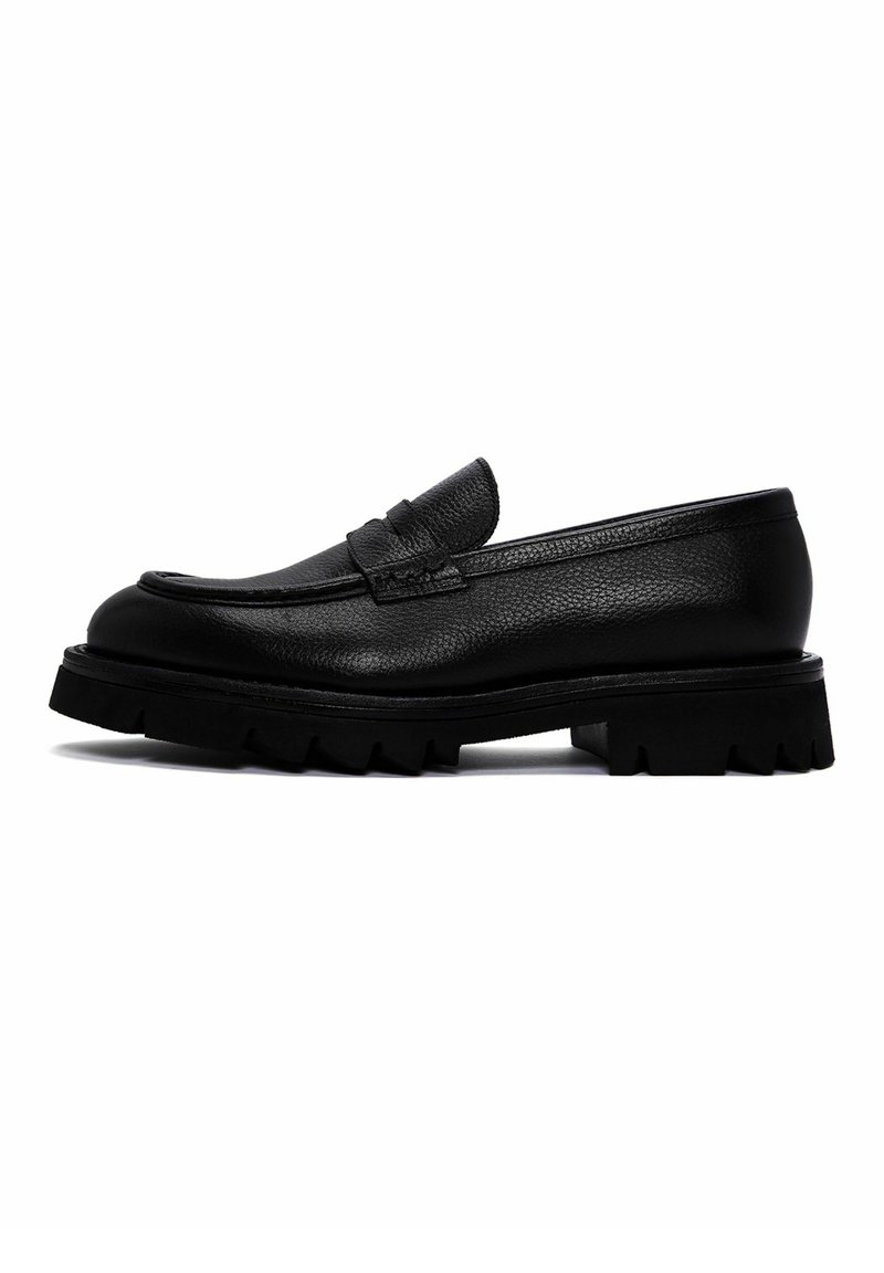 Zwarte leren loafers met een gestructureerde afwerking, een brede band over de wreef en een chunky, ribbelige zool. Het zijaanzicht toont het slanke ontwerp.